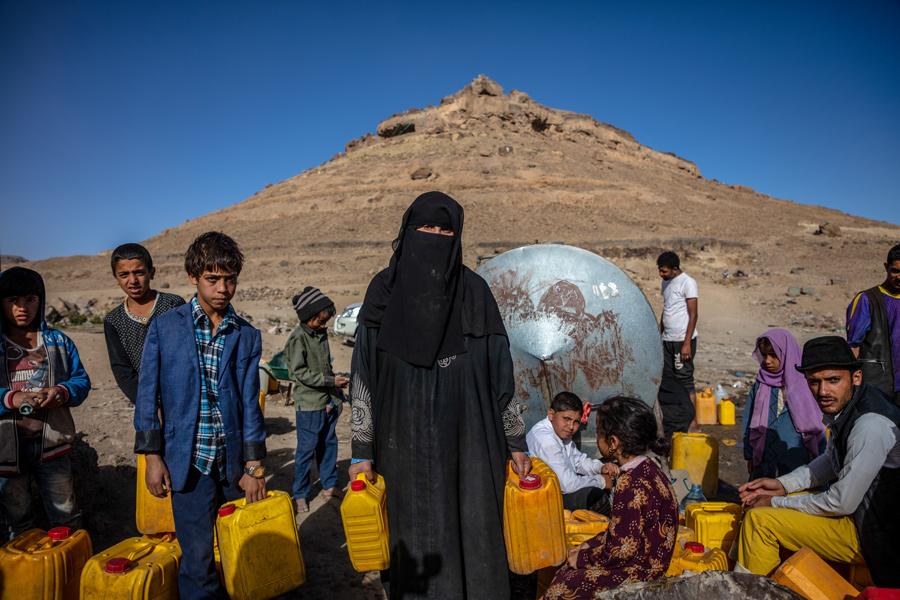 Image of women and children in arid outdoor environment in Yemen holding water canisters.