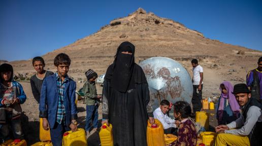 Image of women and children in arid outdoor environment in Yemen holding water canisters. 